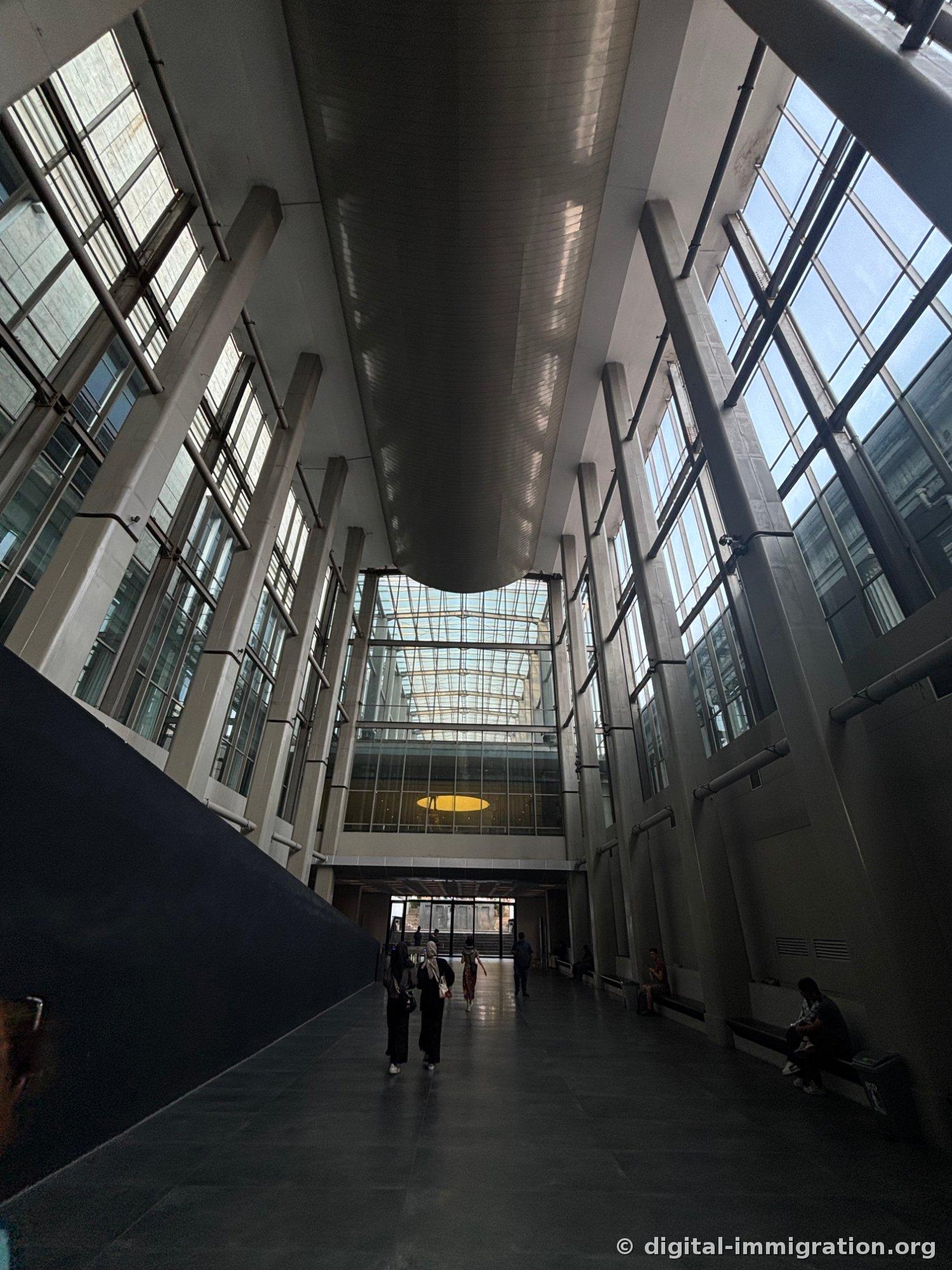 The new wing atrium corridor with long skylight, tall concrete pillars, and large windows with visitors walking