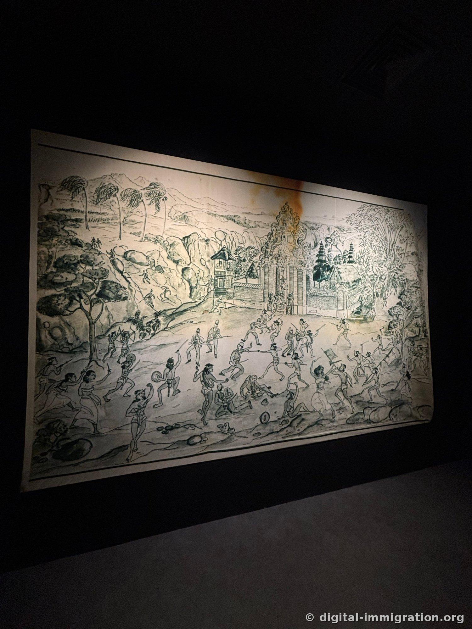 A large paper painting illuminated on the wall of a dark exhibition room, depicting a battle scene before a Balinese temple gateway with armed fighters and soldiers