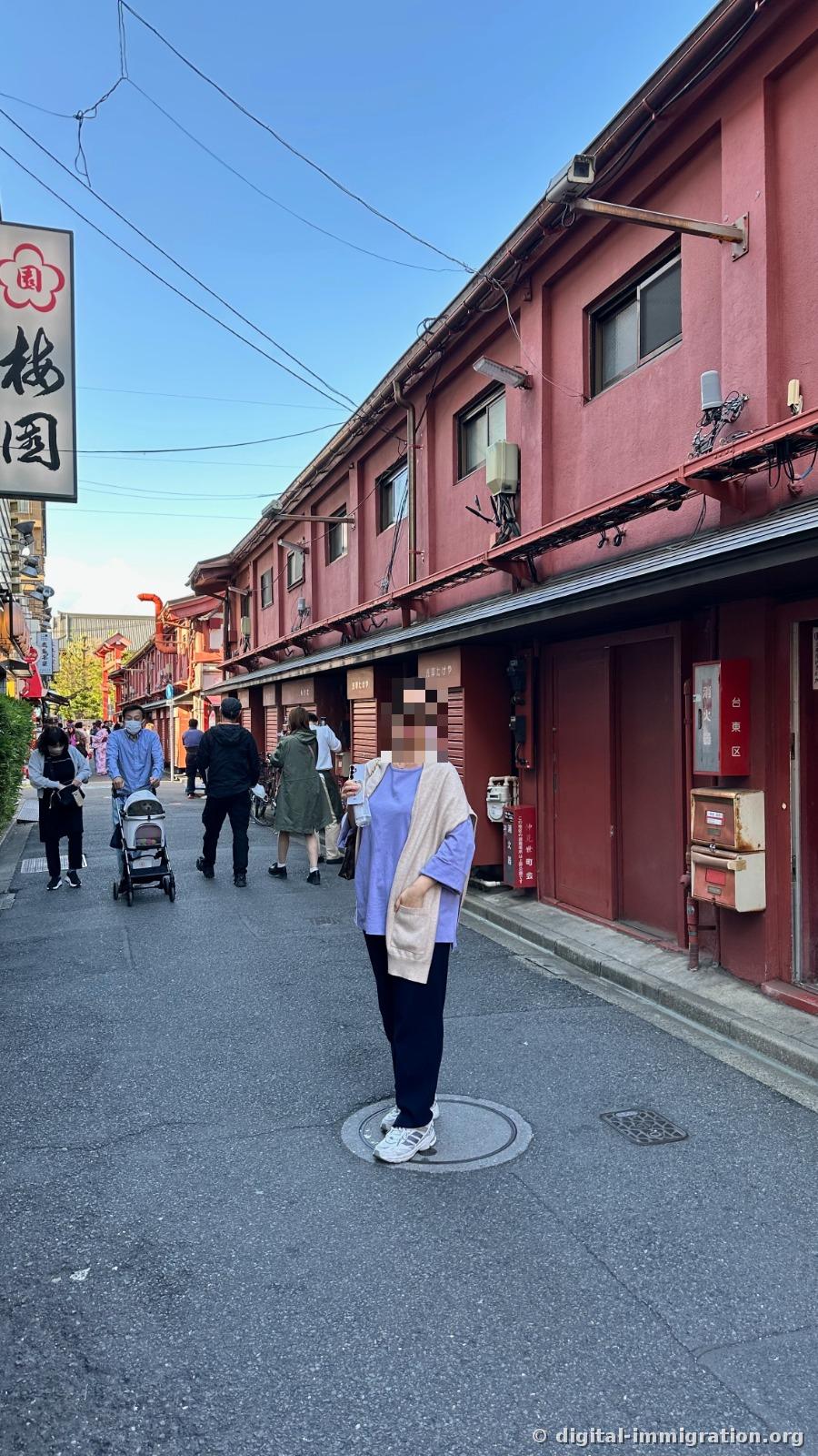 Quiet alley lined with red wooden storefronts, with the 梅園 sign hanging in the upper left