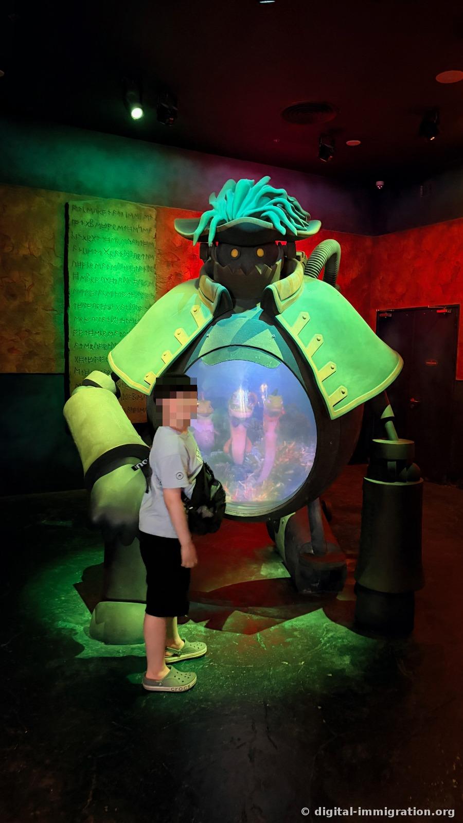 A child standing next to a large diver sculpture bathed in green light, with a small tank visible inside the helmet