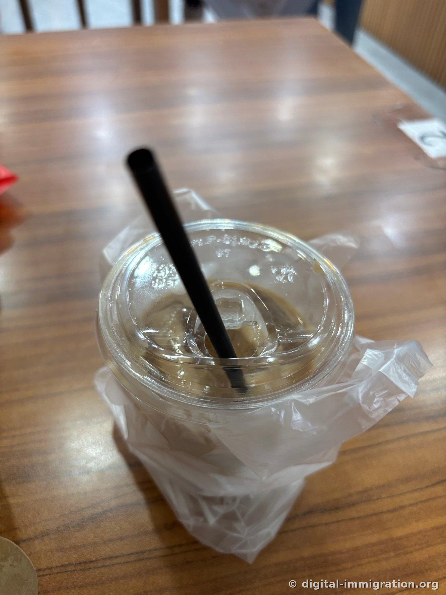 Café au lait glacé sur une table en bois. Une paille noire dépasse d'une tasse en plastique transparent et un sac plastique l'enveloppe par le bas