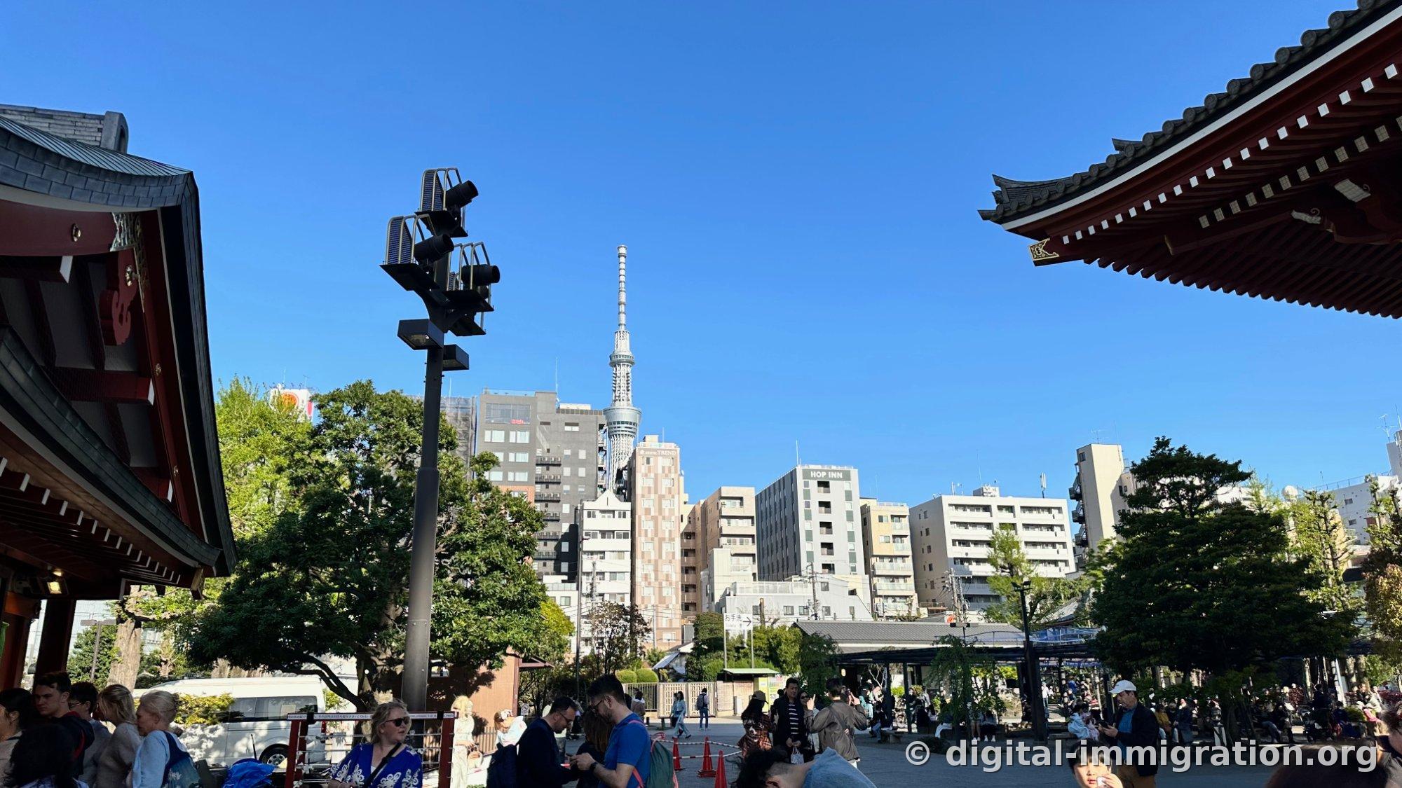 Tokyo Skytree visible between the temple eaves, with surrounding buildings and blue sky at the Senso-ji grounds