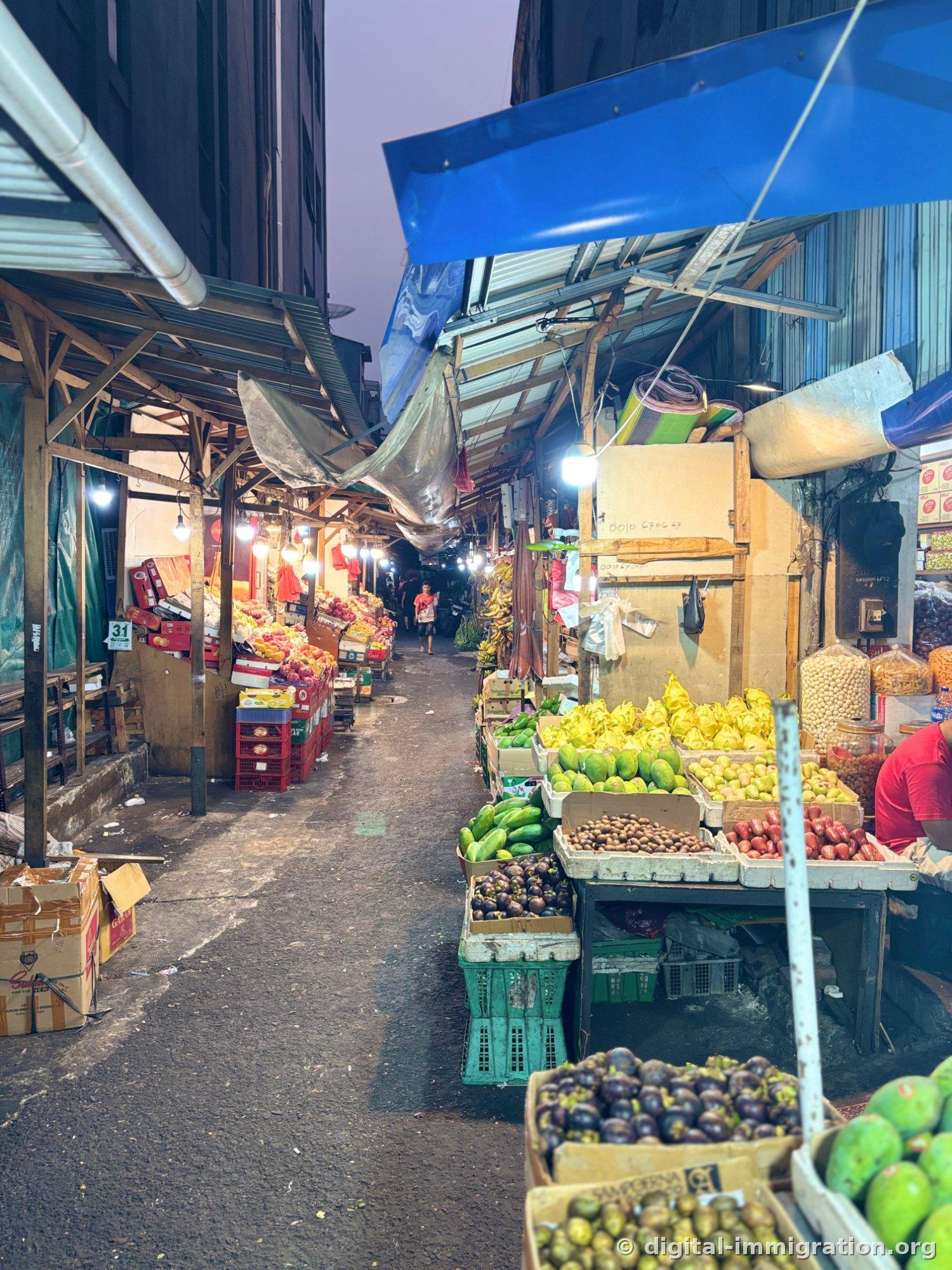 Traditional market alley with blue tarps and corrugated metal roofs, fruit stalls stacked with boxes of yellow-skinned dragon fruit, mangosteens, apples, papaya, and salak