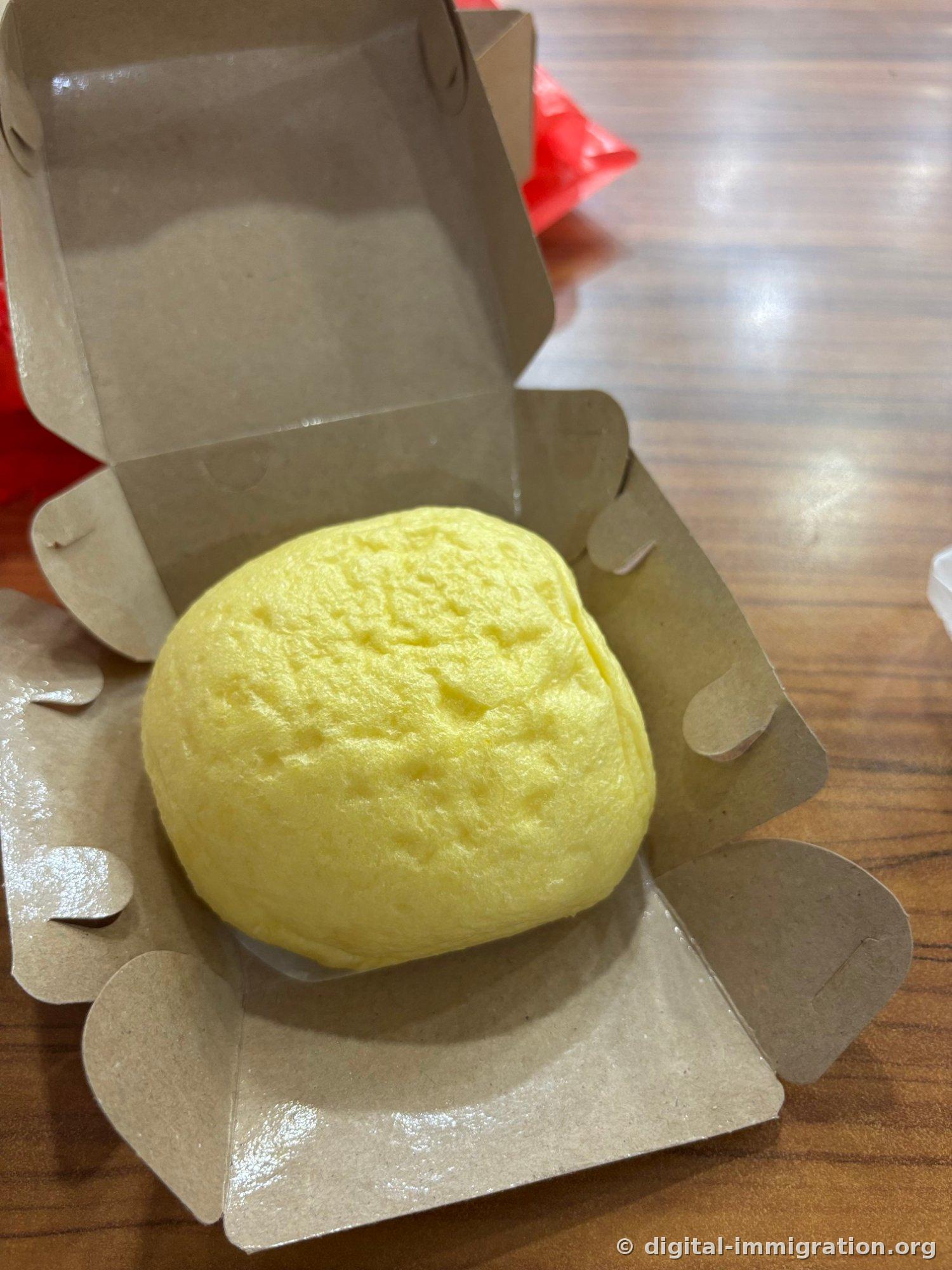 Quand vous ouvrez la boîte en papier, un baozi à la courge jaune lisse sort. À côté se trouve un sac plastique rouge