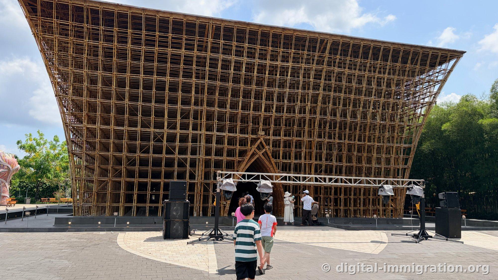 Front of a massive curved bamboo lattice roof building with stage lighting trusses being installed in front