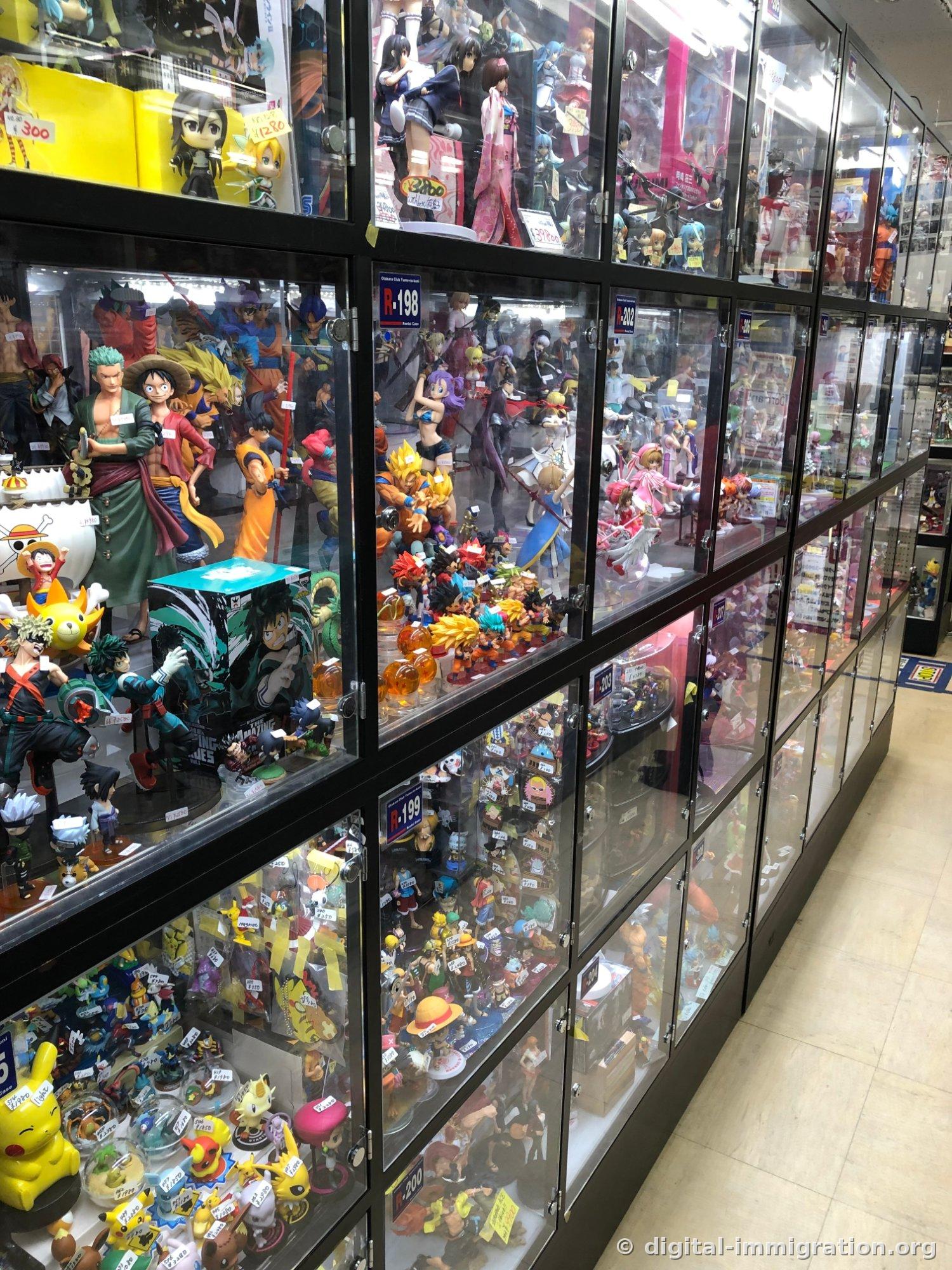 Used figure shop aisle with numbered glass showcases lining the wall, One Piece and Dragon Ball figures