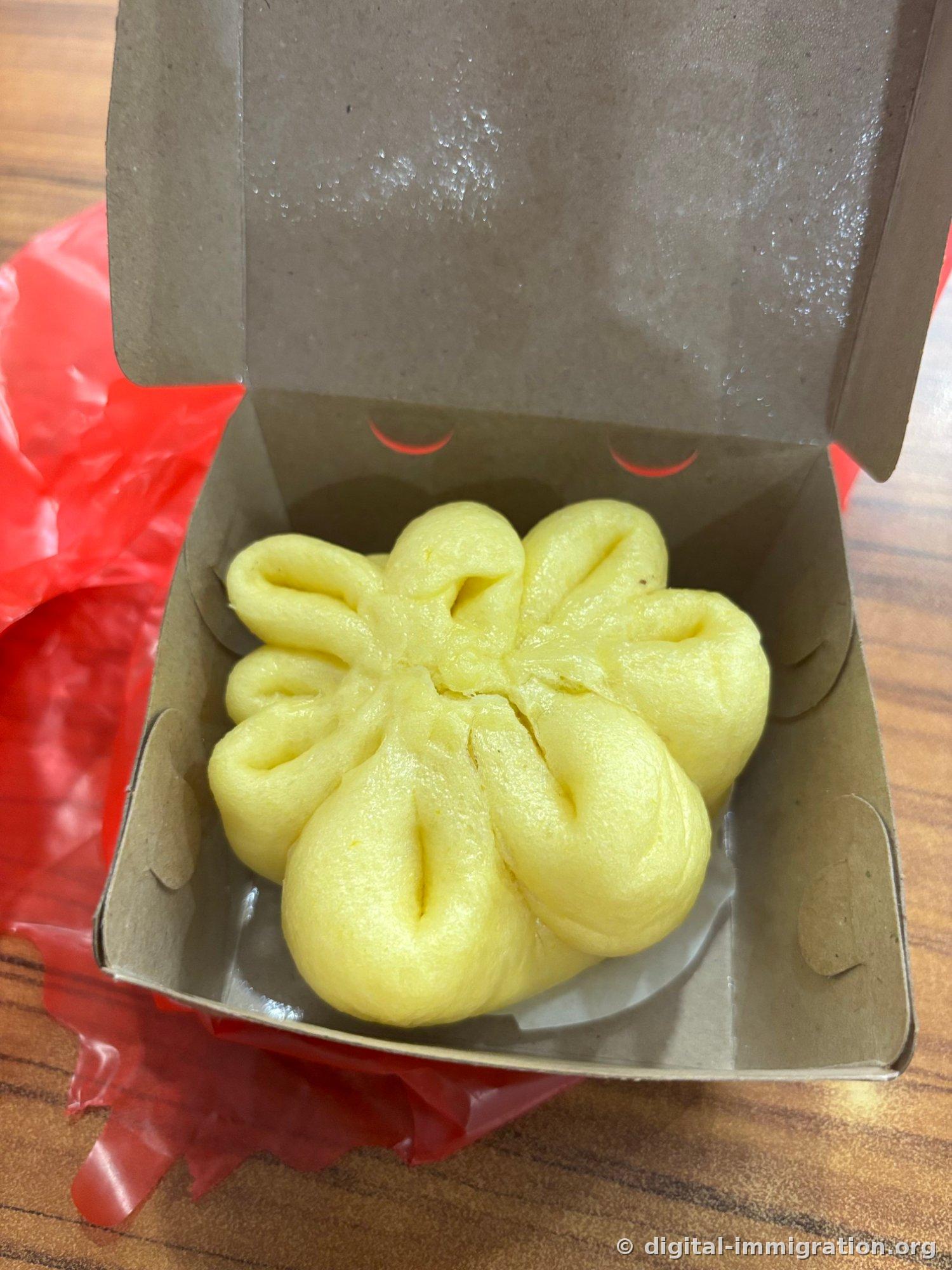 À l'intérieur d'une boîte en papier, un baozi jaune façonné avec des plis comme des pétales de fleur