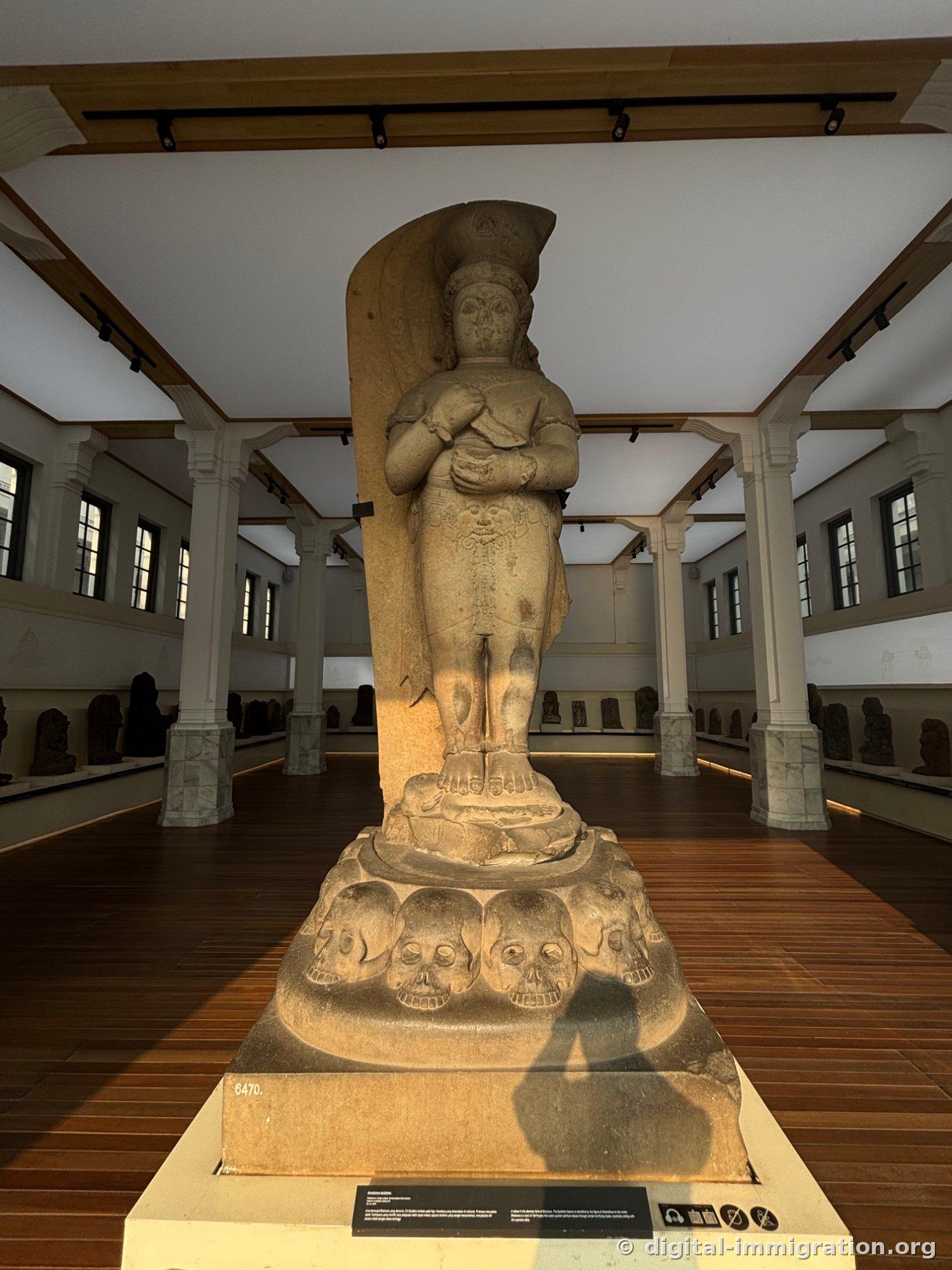 A large stone statue standing in the center of a hall with white columns, with five skulls carved in sequence on the base