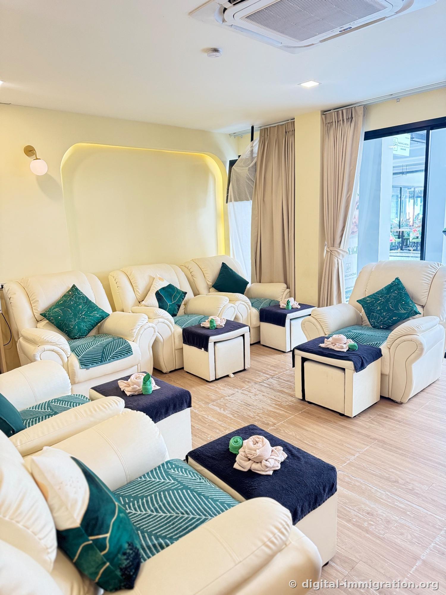 Multiple cream-colored leather recliners and green palm leaf cushions with navy ottomans topped with towels rolled into rose shapes in the foot massage lounge interior