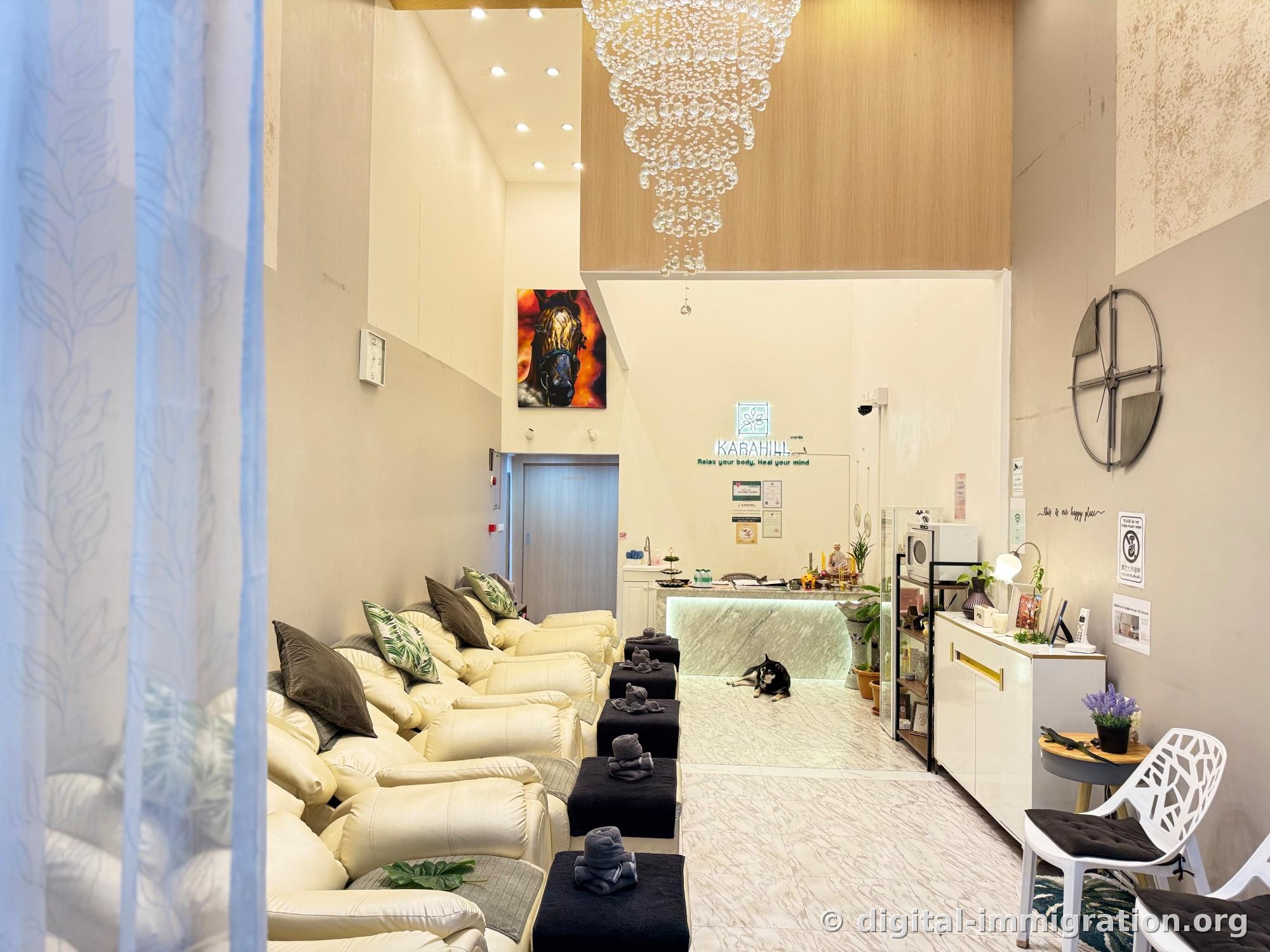 Hall with cream-colored foot massage sofas in a row, glass bead chandelier and horse painting, black Shiba Inu lying on the floor in front of the marble counter inside