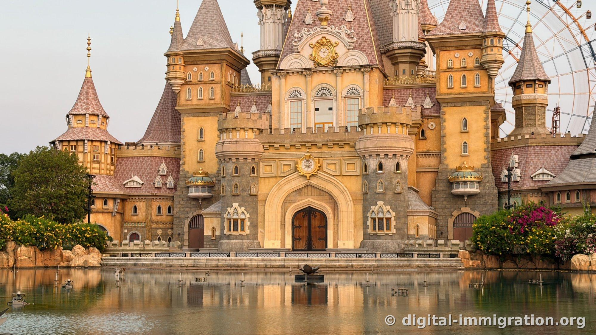 Close-up of the castle facade bathed in orange light at sunset, with part of the ferris wheel on the right