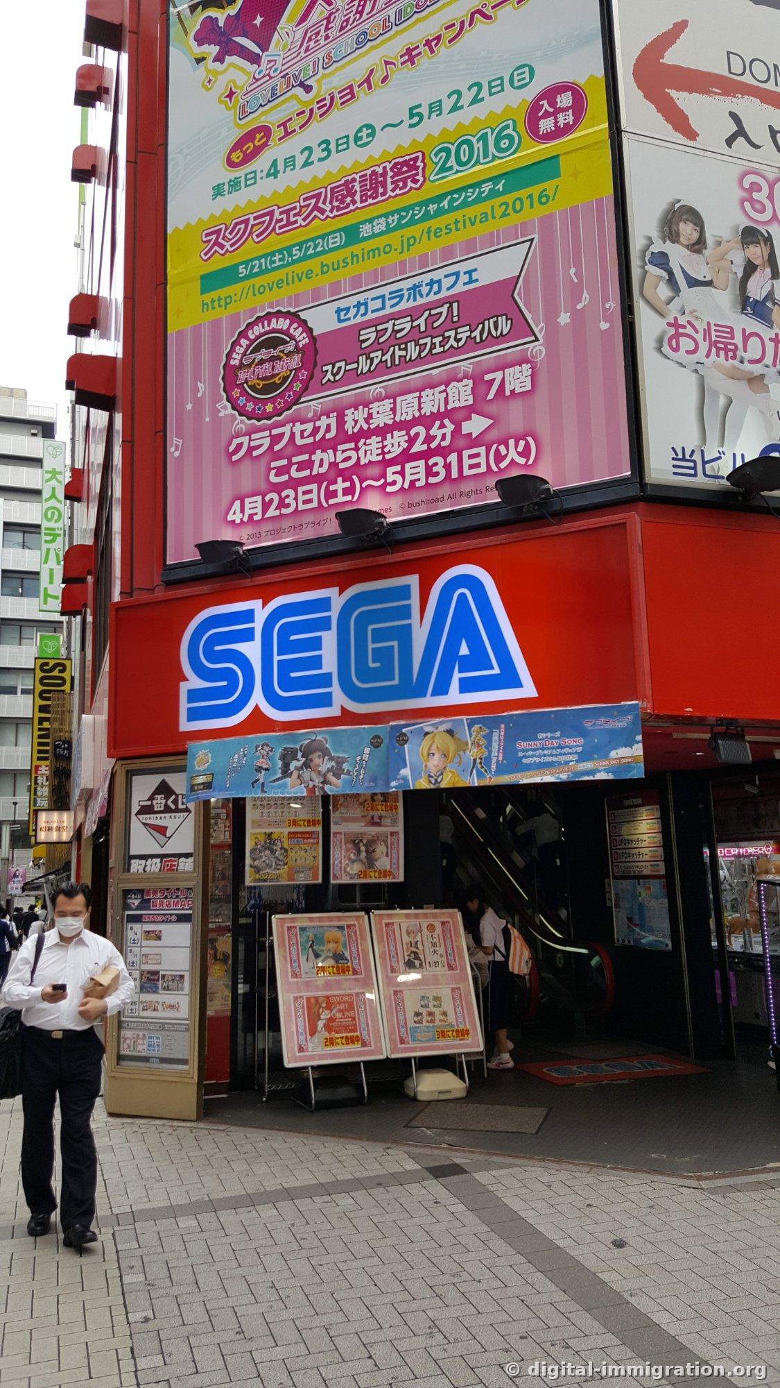 Game center entrance with blue SEGA logo and large collaboration cafe advertisement above