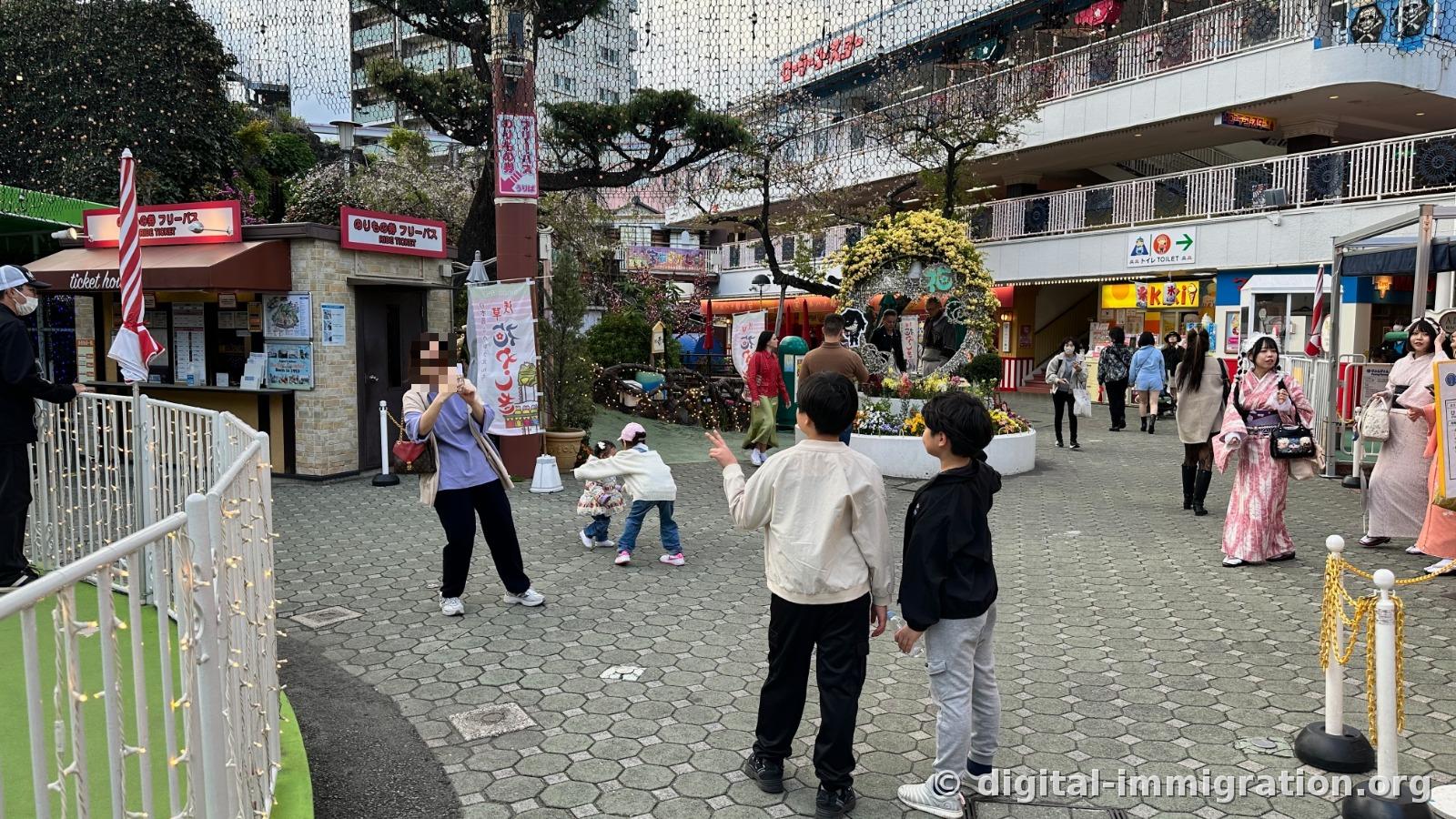 Hanayashiki inner plaza with pass sales booths, flower bed sculptures, kimono-wearing visitors and children playing