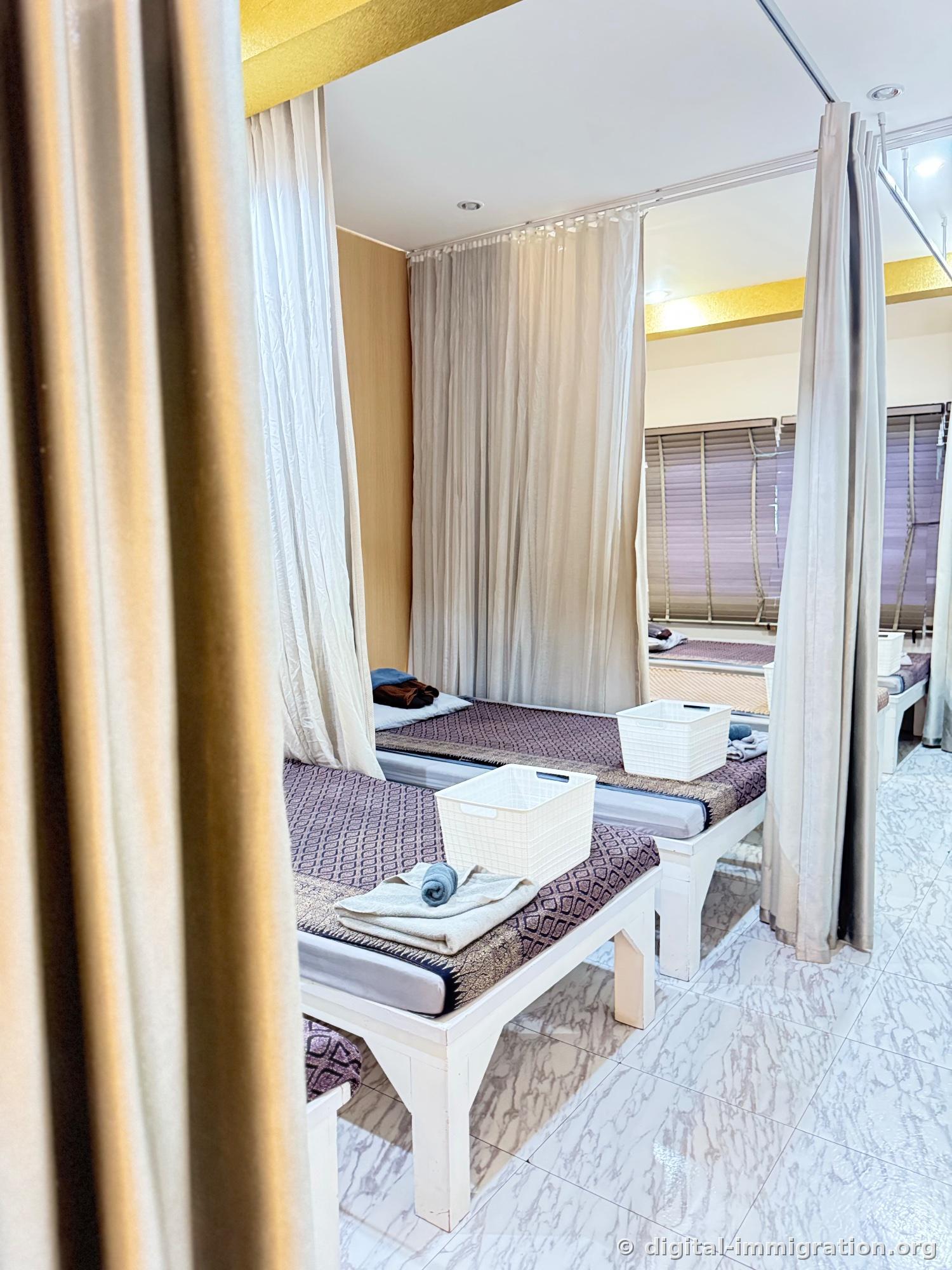 Second floor Thai massage area partitioned by curtains, low wooden bed with purple patterned mat, white basket and rolled towel on the bed