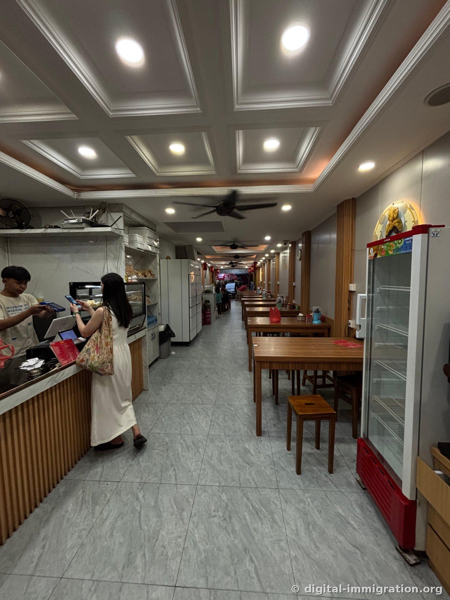 Intérieur du café. Un client paie avec son téléphone à la caisse à gauche, des tables en bois s'étendent à droite et des ventilateurs de plafond pendent au-dessus