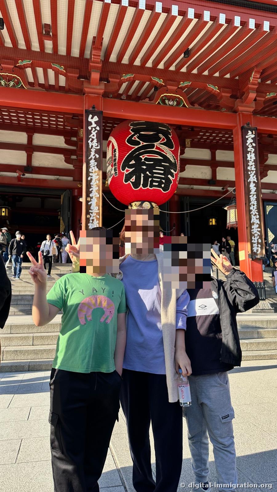 Three people making peace signs on the stairs under the '小舟町' red lantern at Hozomon