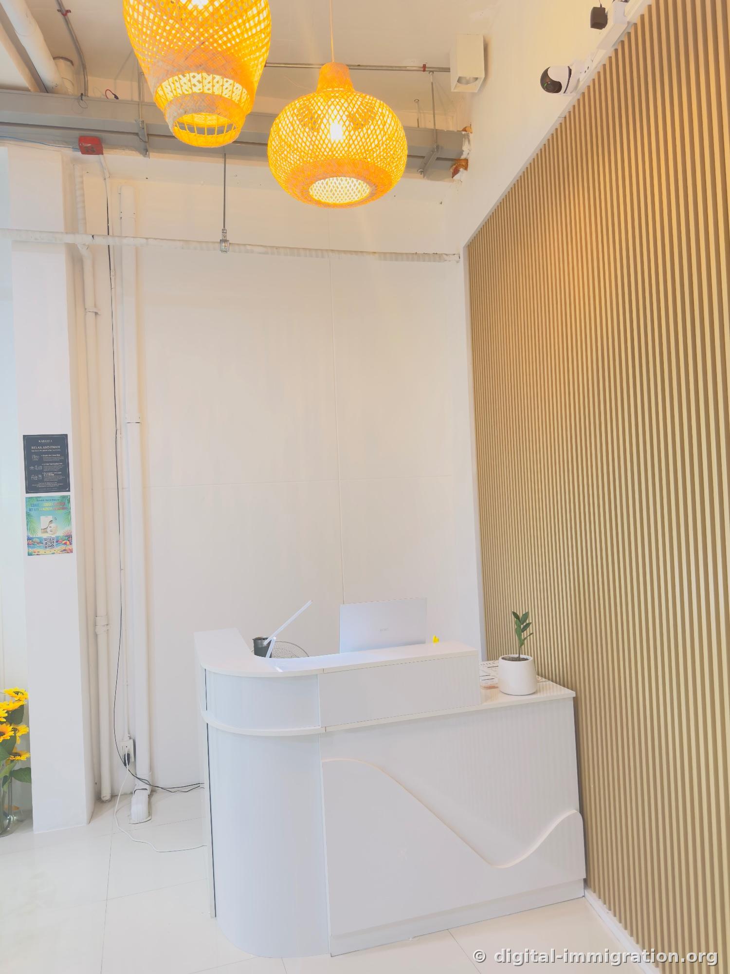 Entrance reception with two rattan pendant lights, white curved desk with laptop and plant, hygiene notice poster and QR promotion poster on left wall