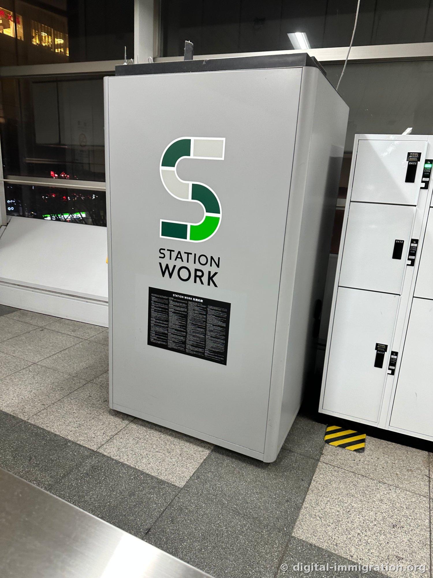 Gray STATION WORK single-person booth inside the station with white numbered coin locker beside it