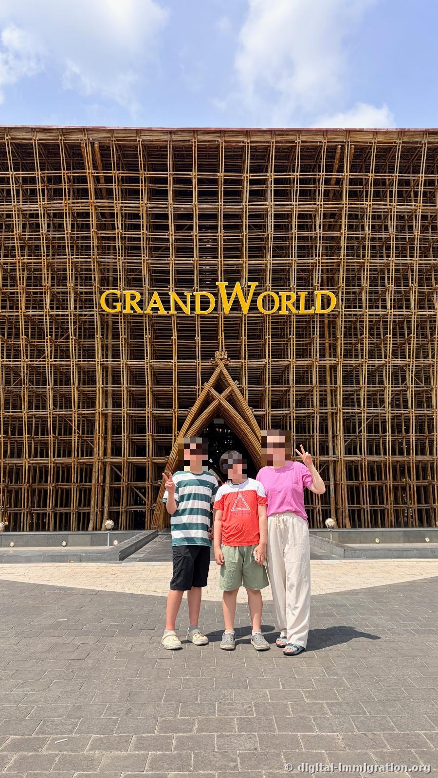 Three people posing with a V-sign in front of a bamboo structure with golden GRAND WORLD lettering
