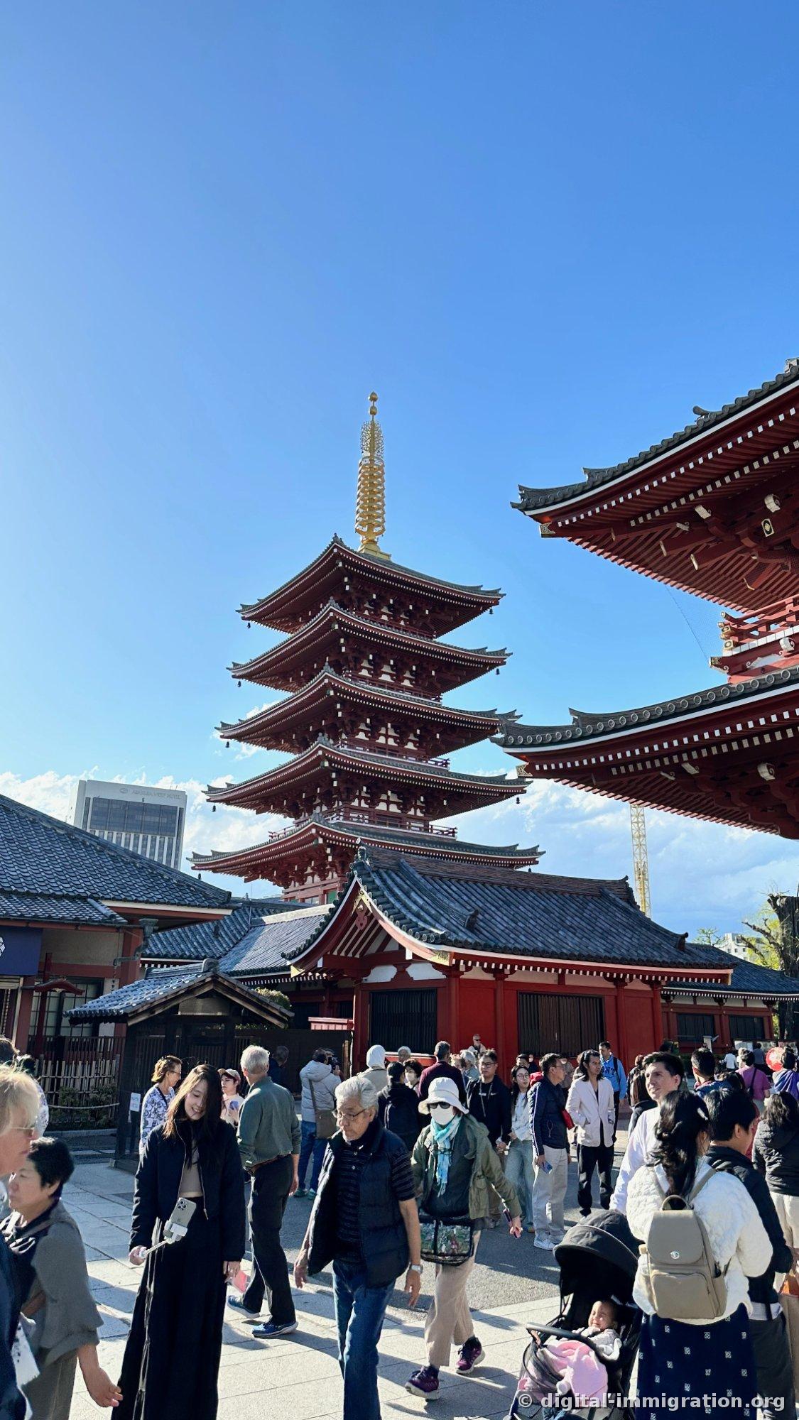 The red five-story pagoda and main hall eaves visible against a blue sky, with tourists passing below