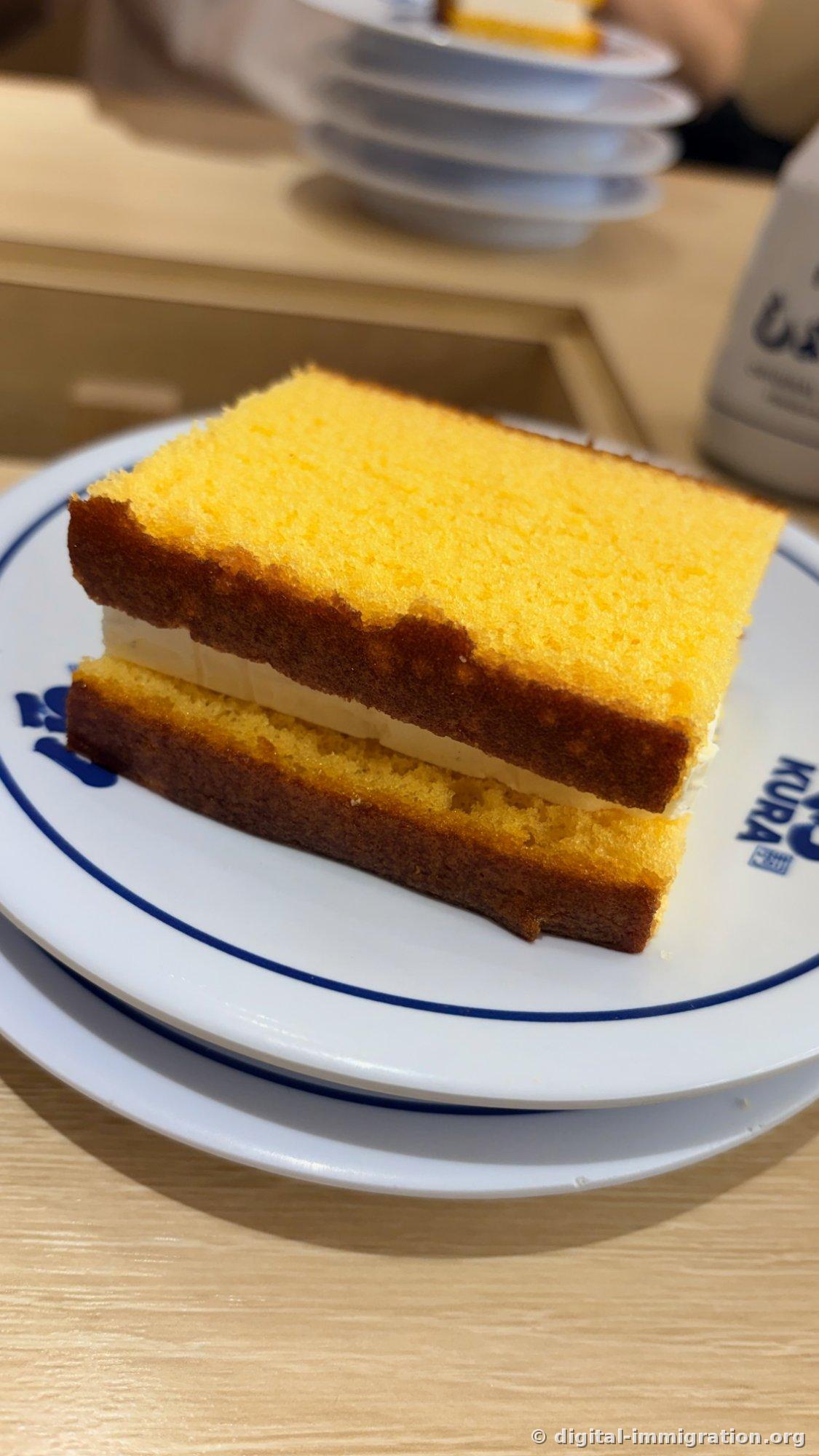 Gâteau Castella vu de haut. La texture jaune de l'éponge est claire et plusieurs assiettes vides sont empilées à l'arrière