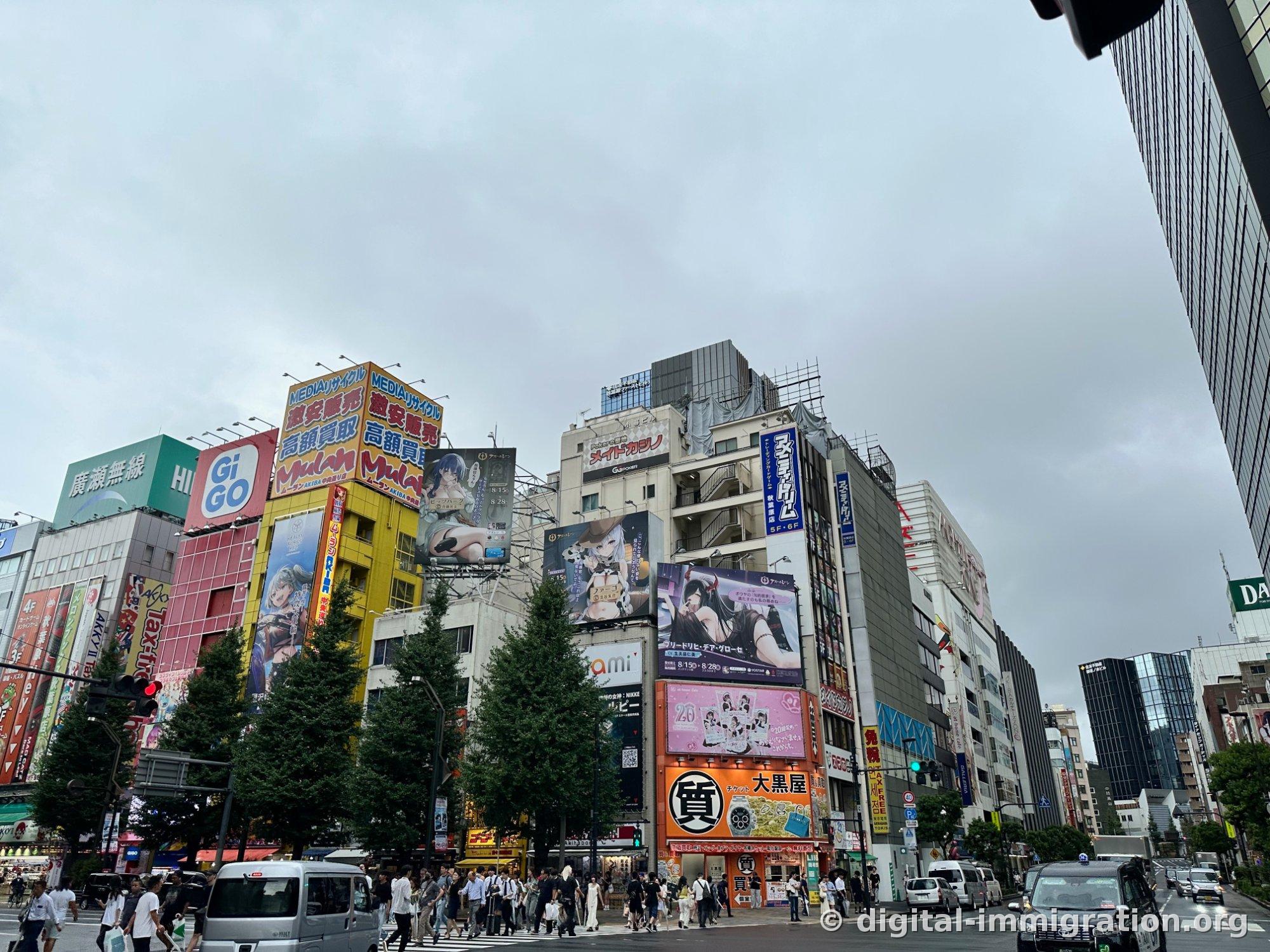 Overcast daytime Akihabara intersection showing GiGO and Mulan signs, orange Daikokuya pawnshop sign