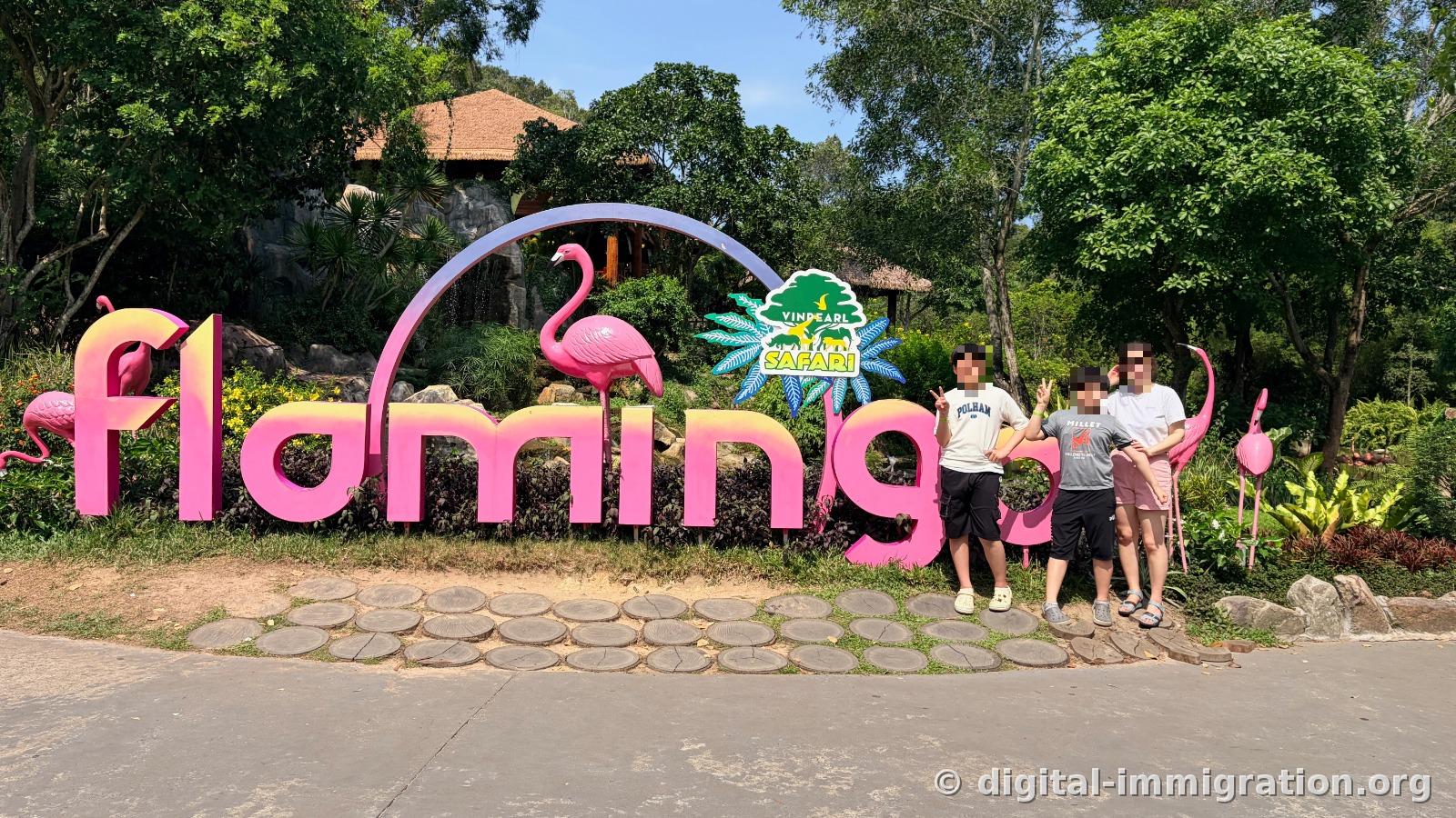 Three children posing with V signs in front of the pink flamingo letter sculpture and Vinpearl Safari logo