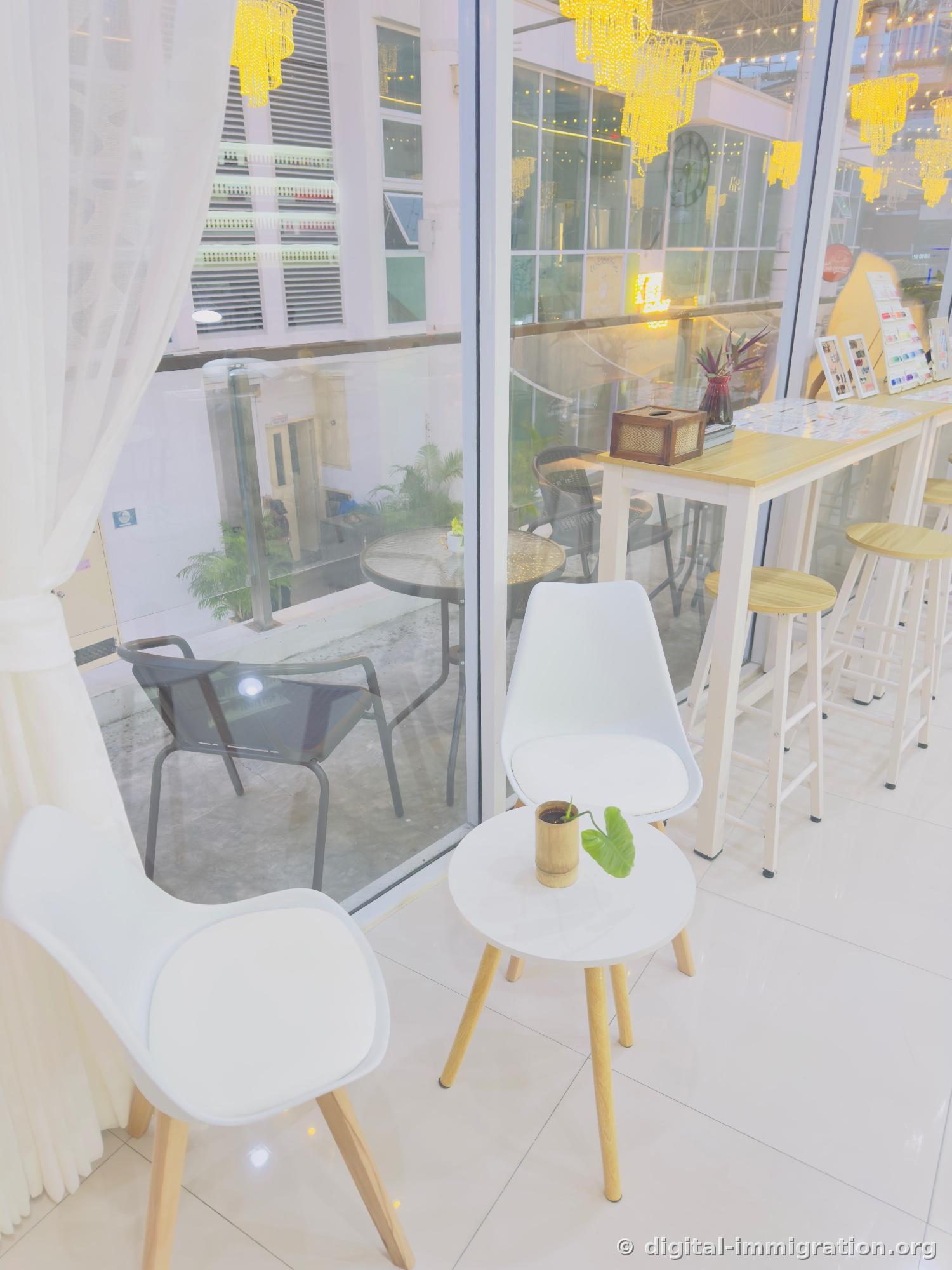 Two white shell chairs by the full-length window with small round table with bamboo vase, natural wood bar table and stool to the right