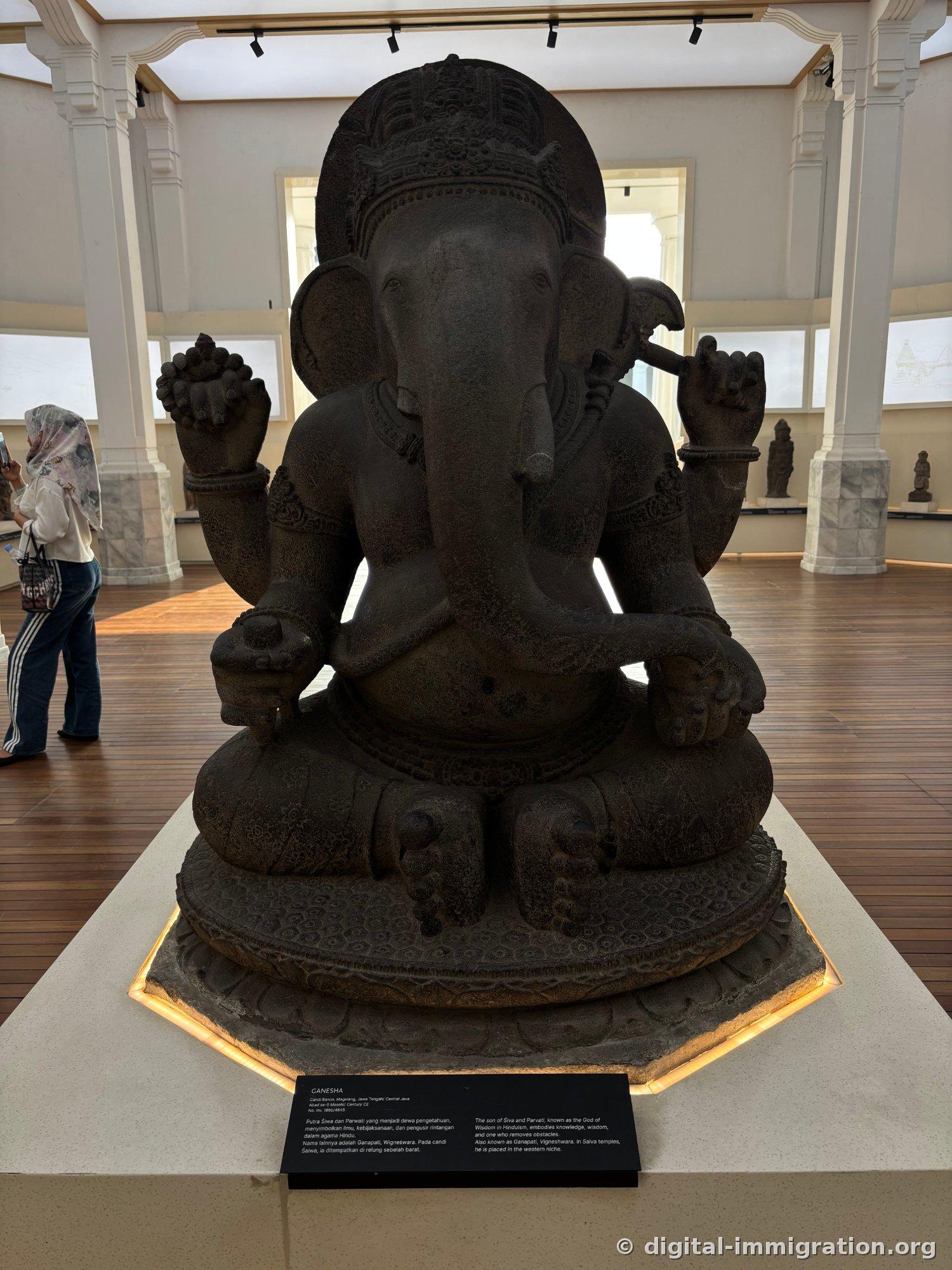 A large volcanic stone seated Ganesha statue with four outstretched arms and indirect lighting beneath the base