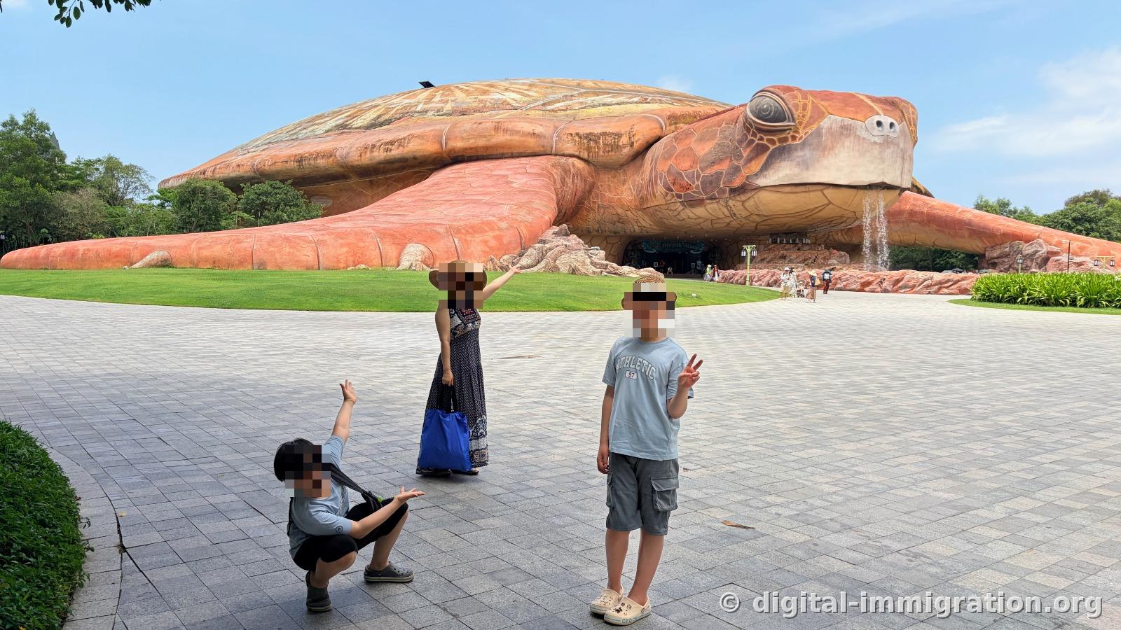A family posing in front of a large red sea turtle-shaped aquarium building on the lawn