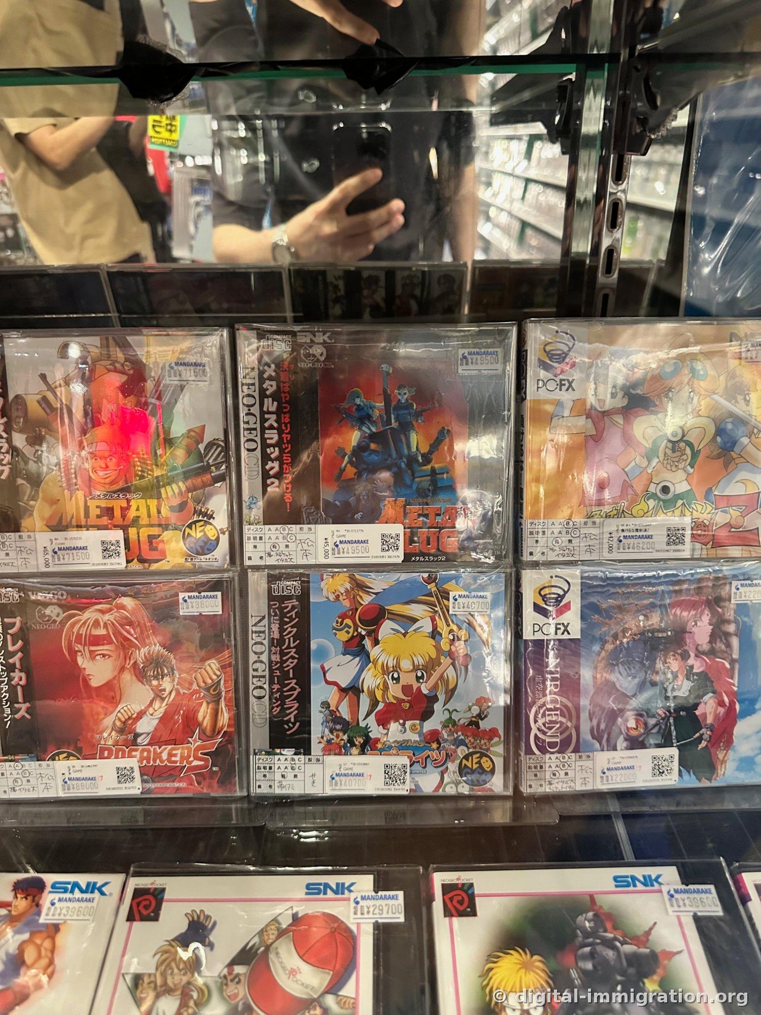 Glass display case with Neo Geo CD Metal Slug, Breakers, PC-FX game packages and Mandarake price tags